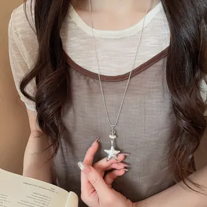 Close-up view of a delicate silver star pendant necklace held by a female model.