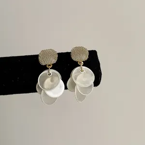 Close-up detail of elegant gold-toned cat's eye earrings with dangling round shell tassels