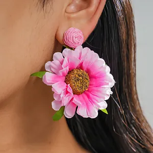 Nahaufnahme von rosa Raffia-Stoff-Blumenohrringen, die Textur und Resort-Stil zeigen
