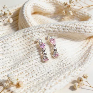 Close-up detail of silver C-shaped earrings with pink heart zircons and rabbit charms