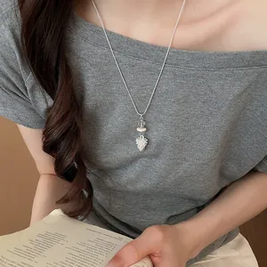 Detailed shot of a minimalist silver floral pendant necklace worn with a stylish grey top.