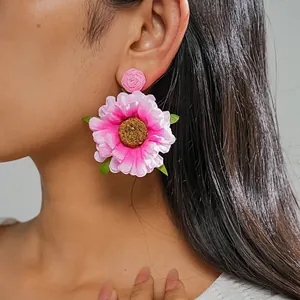 Nahaufnahme von rosa Raffia- und Stoffblumen-Ohrsteckern im Boho-Stil, getragen von einem Model.