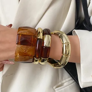 Close-up of Maillard-style acrylic and gold chunky bracelets on a model's wrist.