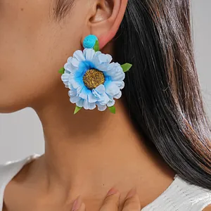 Nahaufnahme eines großen blauen Stoffblumen-Ohrrings mit Bast-Mitte am Ohr eines Modells