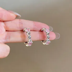 Close-up of silver C-shaped earrings with pink heart-shaped stones on hand for scale