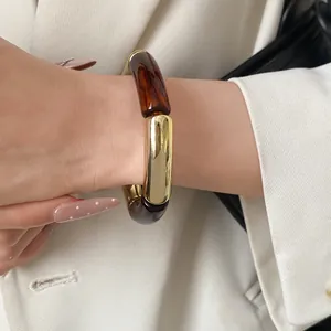 Detailed close-up of a stylish acrylic and gold-toned chunky bracelet on female wrist