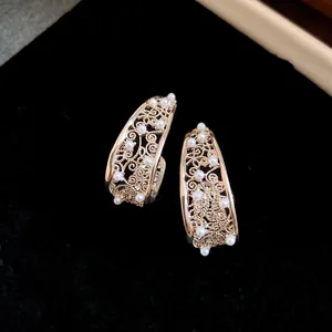 Primo piano di eleganti orecchini a cerchio in oro a forma di C con motivi floreali e perle