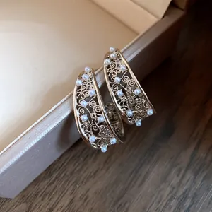 Primo piano di orecchini a C filigranati dorati con accenti di perle