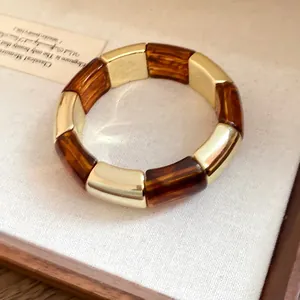 Detailed macro view of amber acrylic and polished gold segmented bracelet with glossy finish