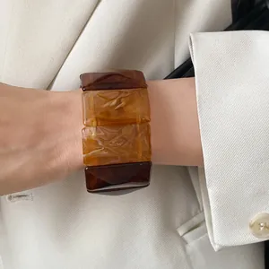 Detailed close-up of a Maillard-style amber acrylic wide bracelet on a model's wrist.
