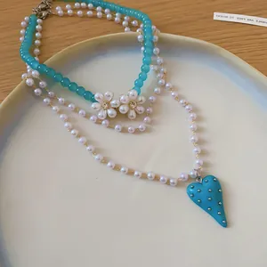 Macro view of a multi-layer pearl necklace featuring a turquoise heart pendant and flowers