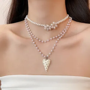 Layered pearl necklace with floral accents and cream heart pendant on female model