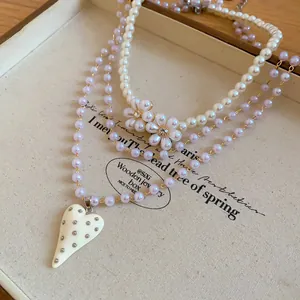 Close-up of multi-layer pearl necklace with heart and flower pendant on jewelry box.