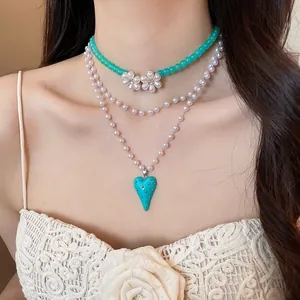 Close-up of a multi-layer pearl necklace with a teal heart pendant and flower details