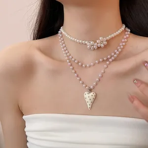 Detail view of a multi-layer pearl necklace featuring delicate flower beads and heart pendant.