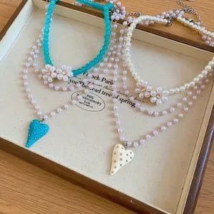 Detailed view of layered beaded necklaces with flower and heart charms in a box.