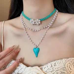 Detail of layered floral beaded necklace with a turquoise heart pendant on a model