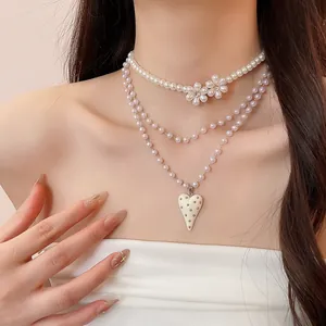 Detail view of a layered white pearl necklace with heart pendant and flower charms.