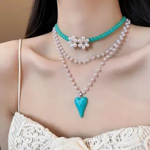 Close-up of a layered necklace featuring turquoise beads, white flowers, and a heart pendant