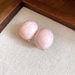 Minimalist pink oval stud earrings with marble texture on a neutral linen fabric