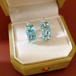 Dettaglio di orecchini a cerchio con zircone blu chiaro quadrato in scatola di velluto.