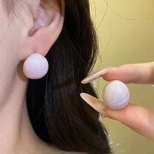 Close-up detail of pink marbled oval stud earrings shown on ear and held by hand