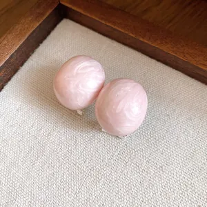 Detailed view of pink oval marble texture earrings on a minimalist linen background