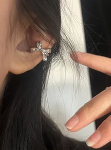 Detailed close-up showing a sparkling silver bow-shaped ear cuff on a woman's ear cartilage.