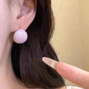 Detail view of a pink oval stud earring with marbled texture on a model's ear