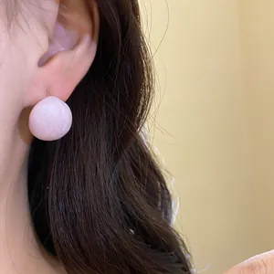Macro view of pink enamel stud earring worn on ear showing marbled texture detail