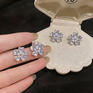 Elegant sparkling zircon flower stud earrings displayed in shell box and held by hand