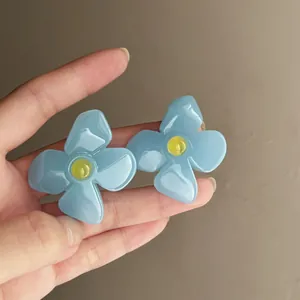 Macro view of vintage blue acrylic flower earrings with yellow details held by hand.