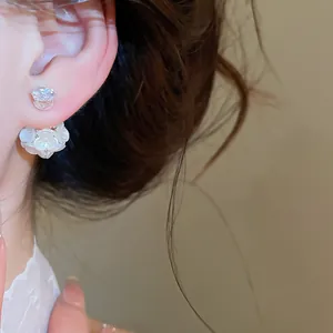 Close-up detail of elegant white flower and crystal front-back stud earrings worn on ear.