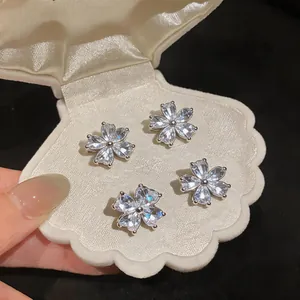 Close-up of four floral zircon stud earrings inside a white shell-shaped velvet jewelry box