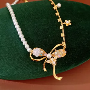 Close-up of elegant pearl and gold chain necklace with a zircon bee and rose bow.