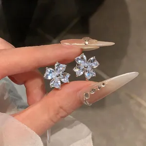 Close-up of silver-tone zircon flower stud earrings held by hand with decorative nails.