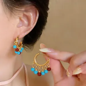 Detail view of 18k gold-plated C-shaped hoop earrings with turquoise and red resin beads.