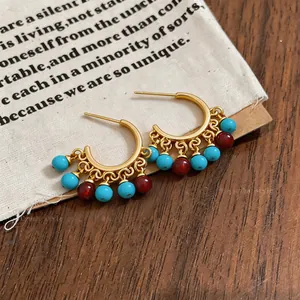 Detail of gold-plated ethnic C-shaped hoop earrings with turquoise and red resin beads