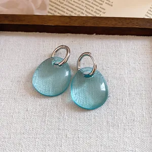 Dettaglio ravvicinato di orecchini ovali in acrilico azzurro con eleganti cerchi in argento.
