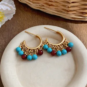 Detailed view of 18k gold plated C-shaped earrings with turquoise and red resin beads