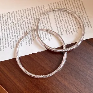 Gros plan de boucles d'oreilles créoles argentées sur fond de papier vintage.
