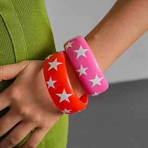 Detailed view of vibrant orange and pink resin star bangles worn over green knit garment
