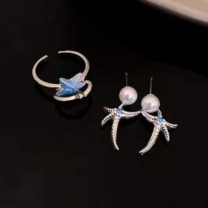 Dettaglio di un elegante anello a stella marina e orecchini di perle con pietre blu.