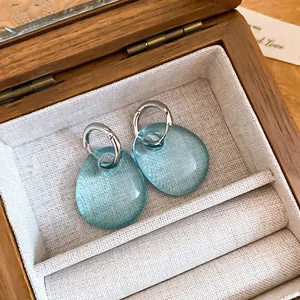 Dettaglio di orecchini a goccia in acrilico blu traslucido in un portagioie di legno