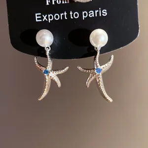 Dettaglio di orecchini a stella marina argentati con perla bianca e zircone blu