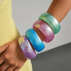 Close-up detail of four colorful iridescent chunky resin bangles on a model's arm.