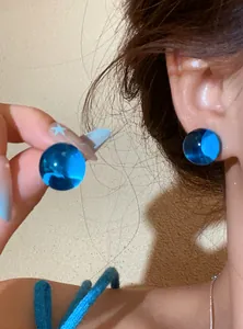 Close-up of translucent bright blue ball earrings shown on model ear with vibrant summer style