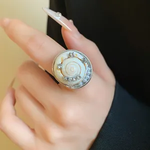Détail d'une bague bohème en coquillage avec perles et strass sur le doigt d'une femme.