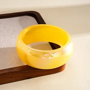 Detail view of yellow iridescent resin bangle with holographic finish on wooden tray