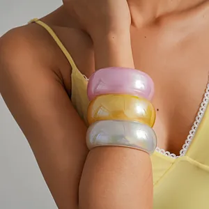 Close-up of three iridescent resin bangles in pink, yellow, and white on a model's arm